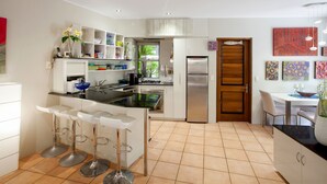 Une cuisine moderne avec des meubles blancs, un réfrigérateur en acier inoxydable et un coin bar équipé de tabourets.