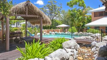 A pool area with lounge chairs, a thatched gazebo, and a rocky landscape.