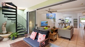 Un salon moderne avec un escalier, des canapés, un coin repas et une cuisine.