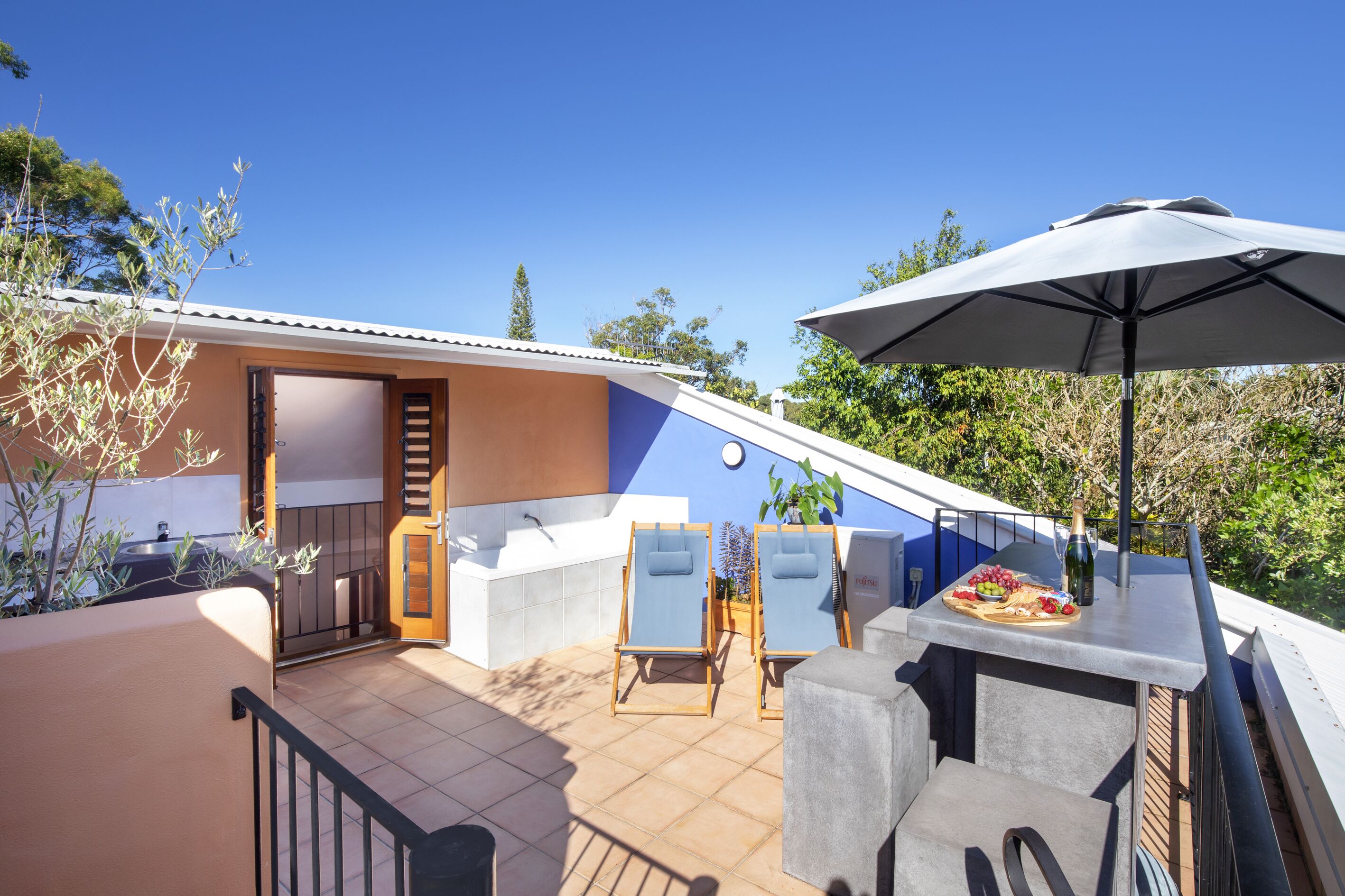 Terraza en la azotea con jacuzzi, sillones de descanso y una mesa con una botella y frutas.