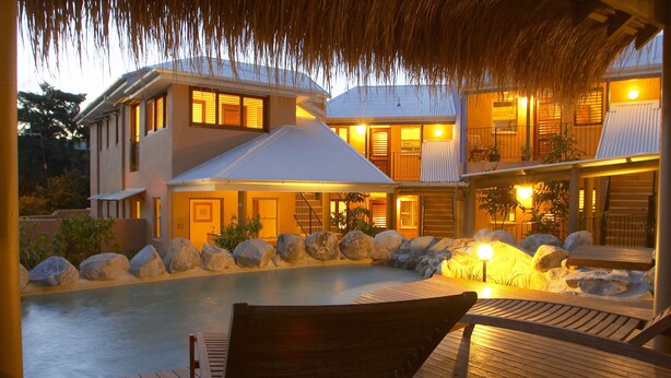 Une maison avec une piscine, une terrasse en bois et un toit de chaume.