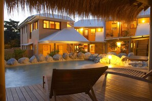 Une maison avec une piscine, une terrasse en bois et un toit de chaume.