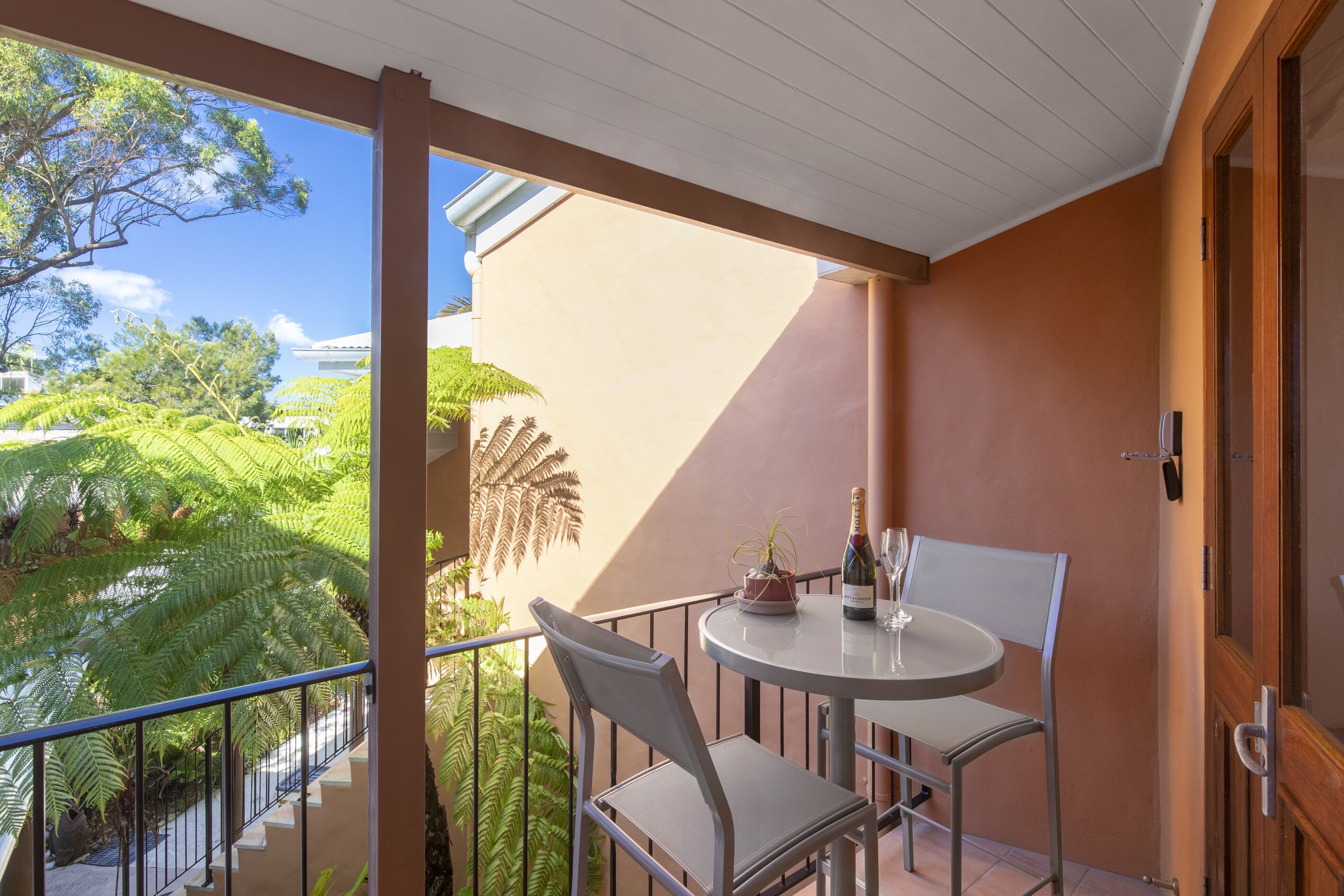 A balcony with a table and chairs, a potted plant, and a bottle of champagne.