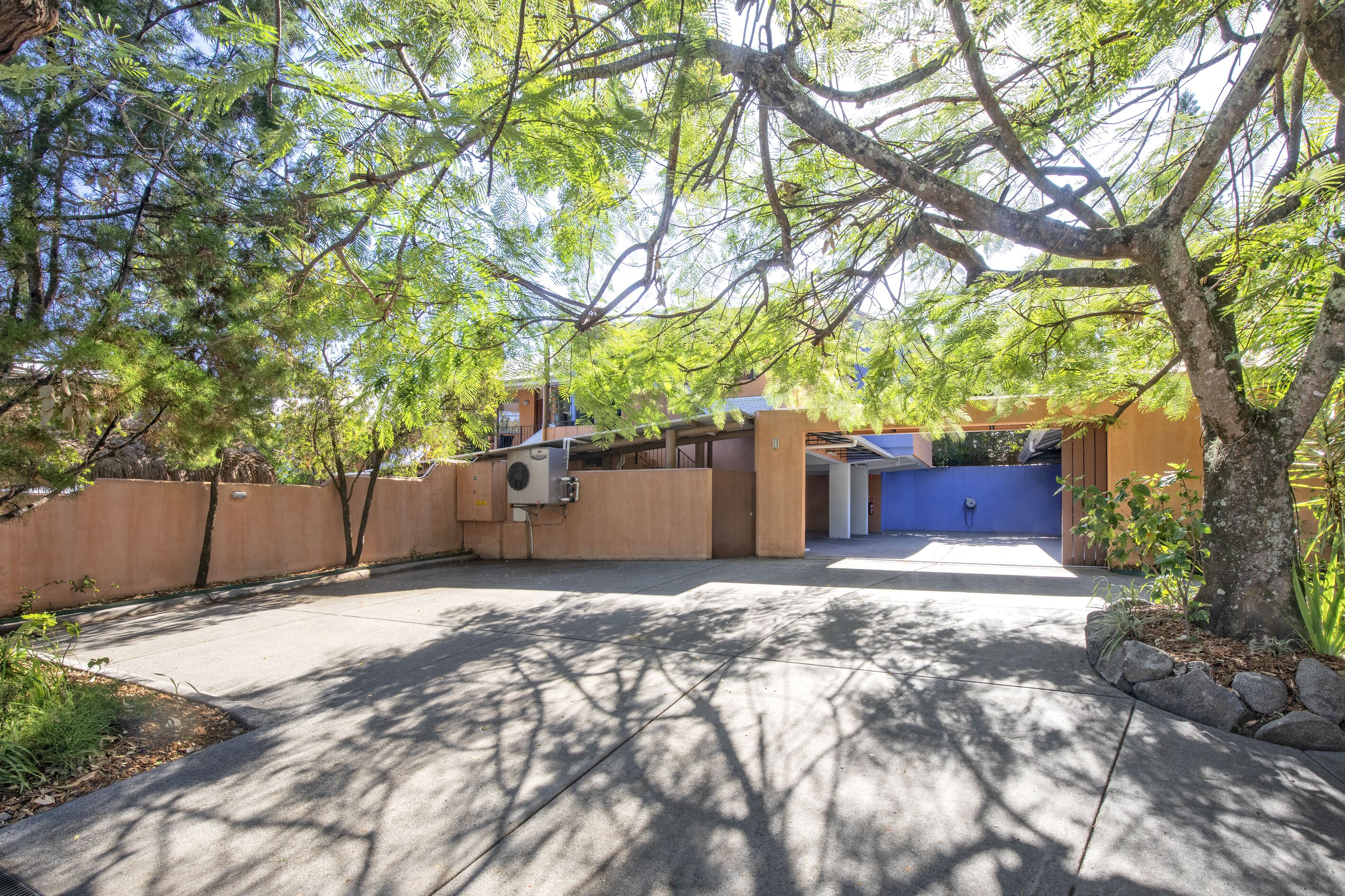 A gated driveway leading to a building with a covered entrance, surrounded by trees and a stone wall.
