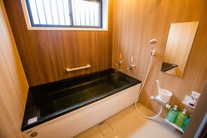 Une salle de bain avec une baignoire noire, une fenêtre, un miroir et une douche.