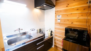 A compact kitchen with a stainless steel sink, dark wooden cabinets, a black range hood, and a built-in microwave. - Shioya Spa (Minakami)