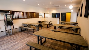 A dining area with multiple wooden tables and benches, a vending machine, and a kitchen area in the background. - Shioya Spa (Minakami)