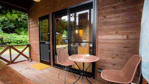A wooden deck with two wicker chairs and a small round table, a glass door leading to a room, and a wooden railing. - Shioya Spa (Minakami)