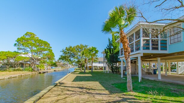 Une propriété située au bord de l’eau, avec un canal, un sentier bordé de verdure et un bâtiment doté d’un balcon donnant sur l’eau.