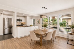 Una cocina moderna con armarios blancos, un refrigerador de acero inoxidable y un comedor con mesa y sillas de madera.