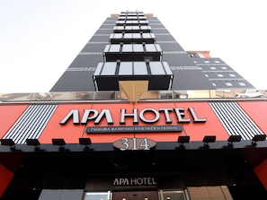 The exterior of the APA Hotel with a modern design, featuring a prominent red facade and the hotel's name displayed in large letters. - APA Hotel Tsukuba-Bampakukinenkoen-Ekimae (Tsukuba)