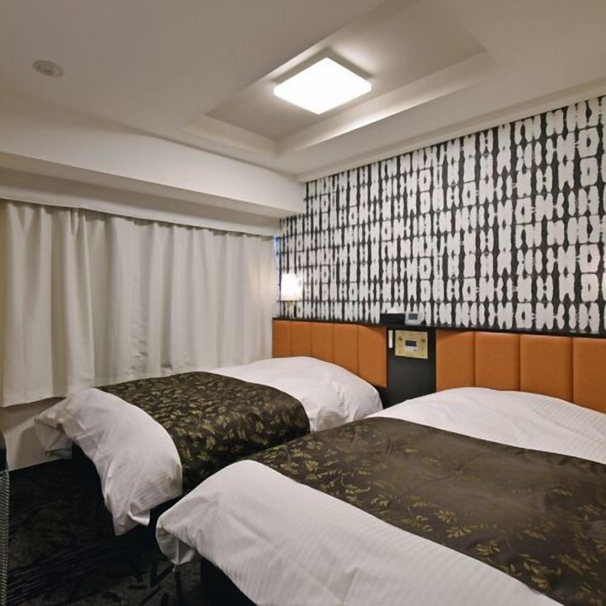 Une chambre d'hôtel avec deux lits, un mur décoré d'un motif, un luminaire au plafond et une table de chevet.