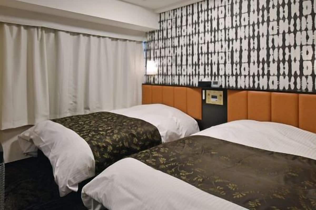 A hotel room with two beds, a patterned wall, a ceiling light, and a nightstand.