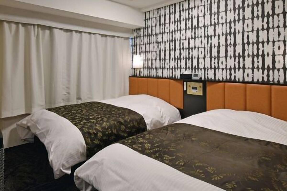 Une chambre d'hôtel avec deux lits, un mur décoré d'un motif, un luminaire au plafond et une table de chevet.
