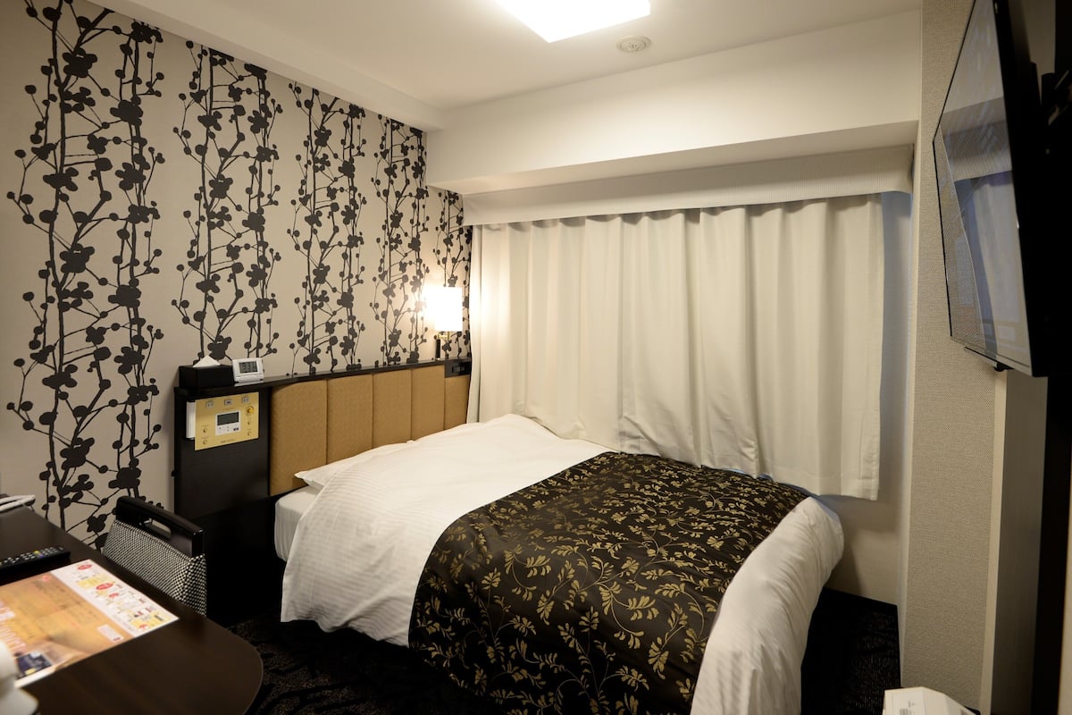 A hotel room with a bed, a desk, a lamp, and a TV.