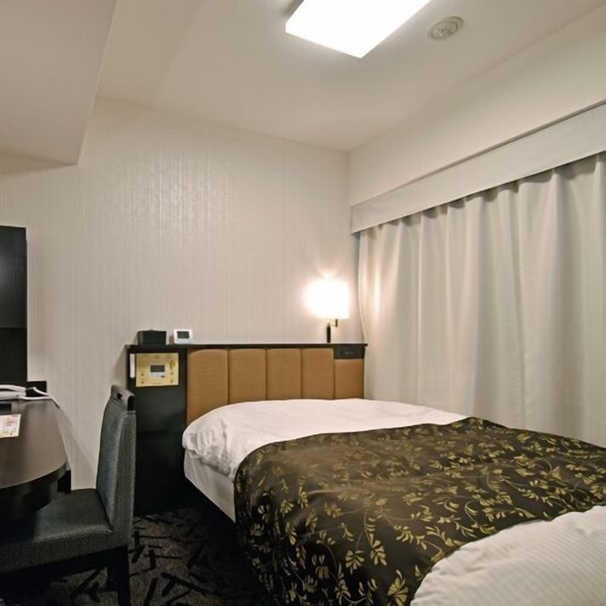 Une chambre d’hôtel comprenant un lit, un bureau, une chaise, une table de chevet et une lampe.