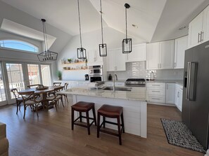 Una cocina amplia con una isla grande, armarios blancos e iluminación colgante.