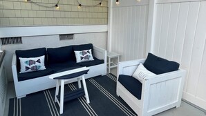 Ein heller Sitzbereich im Freien mit einer Couch und einem Sessel, einem kleinen Tisch und Lichterketten.