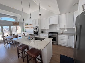 Een moderne keuken met witte kastjes, roestvrijstalen apparatuur en een groot eiland met barkrukken.