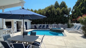 Ein Garten mit Swimmingpool, Liegestühlen, einem Tisch mit Stühlen und einer überdachten Terrasse.