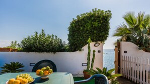 A table with a bowl of fruit and a chair, a potted plant, and a view of the sea. - Blumarine house on the sea, parking and wi.fi (Avola)