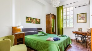 A bedroom with a green bedspread, a wooden wardrobe, a green chair, and a desk with drawers. - Blumarine house on the sea, parking and wi.fi (Avola)