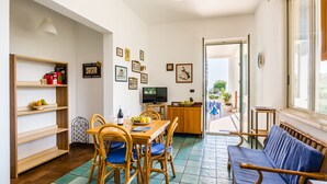 A dining area with a wooden table, chairs, and a television. There are shelves with books and decorative items on the wall. - Blumarine house on the sea, parking and wi.fi (Avola)