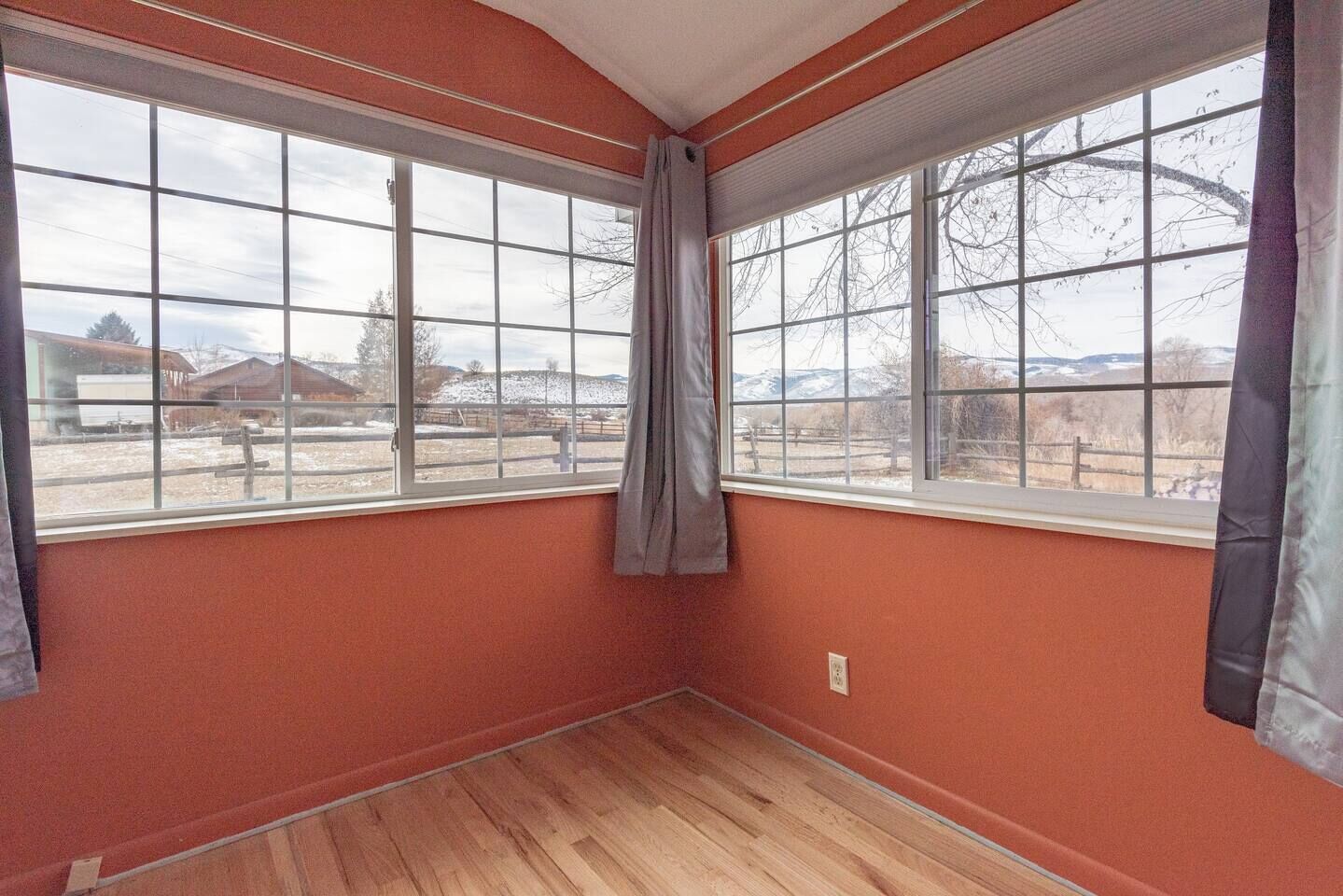 A room with two large windows, wooden flooring, and a plain orange wall.