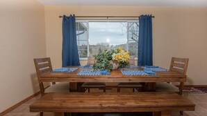 A dining area with a wooden table, blue placemats, and chairs. A basket of yellow flowers is on the table. - Wind River Place- Mountain views, Cozy nights, Sleeps 6! (Lander)