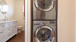 A compact laundry area with two front-loading washing machines and a white vanity with a sink and mirror. - Wind River Place- Mountain views, Cozy nights, Sleeps 6! (Lander)