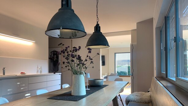 A modern kitchen with a wooden countertop, two pendant lights, a vase with flowers, and a view of the outdoors through a window.