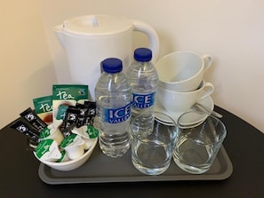 Een dienblad met theezakjes, waterflesjes, een waterkoker en bekers.
