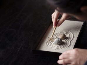 A person using a wooden tool to rake sand in a rectangular container, creating patterns. - ZEN&BED Bogetsu-An (Koshu)