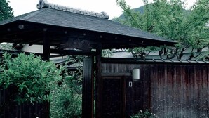 A traditional wooden structure with a tiled roof, surrounded by lush greenery and a stone pathway. - ZEN&BED Bogetsu-An (Koshu)