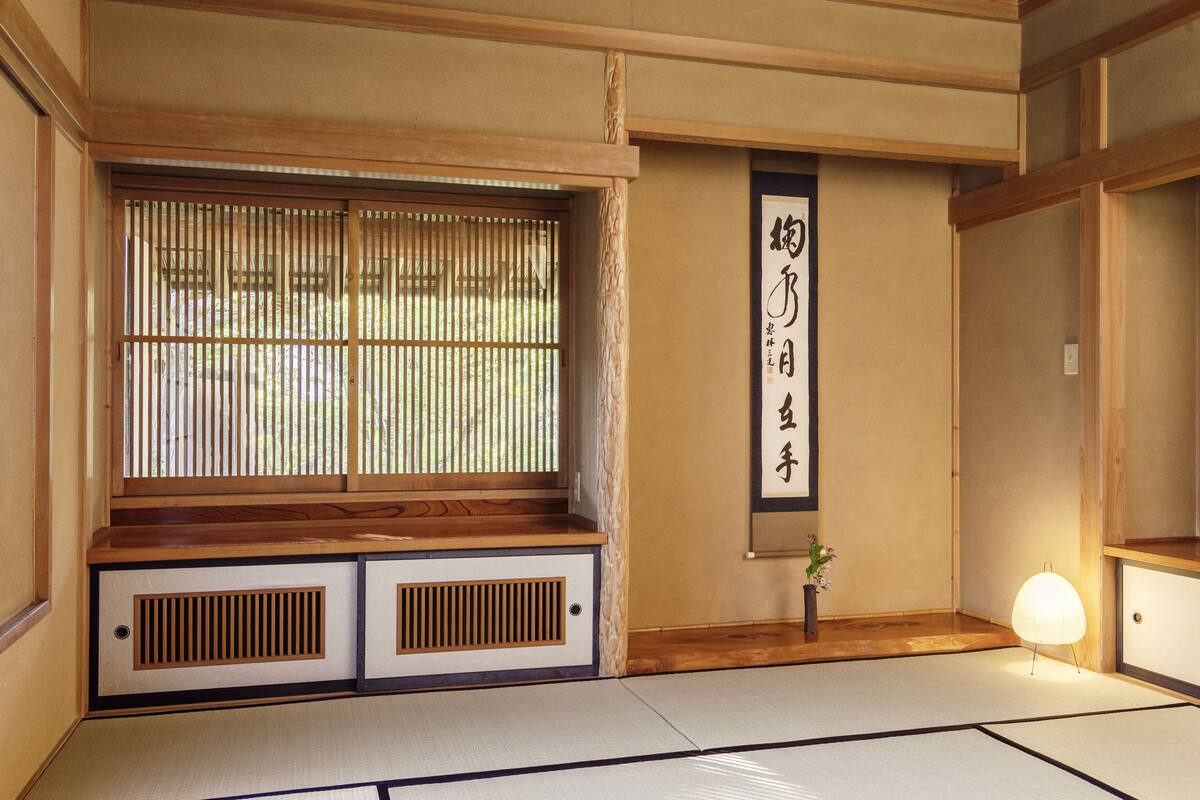 A traditional Japanese room with tatami flooring, a sliding door, a shoji screen, and a calligraphy scroll.