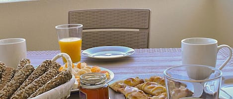A table set with breakfast items including bread, pastries, and drinks, overlooking a beach.