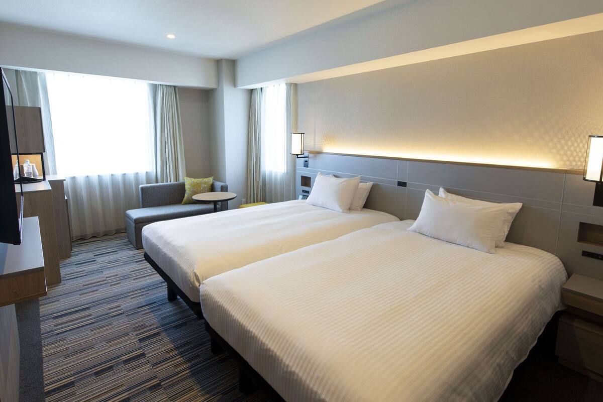 A hotel room with two beds, a sofa, a small table, and a TV.