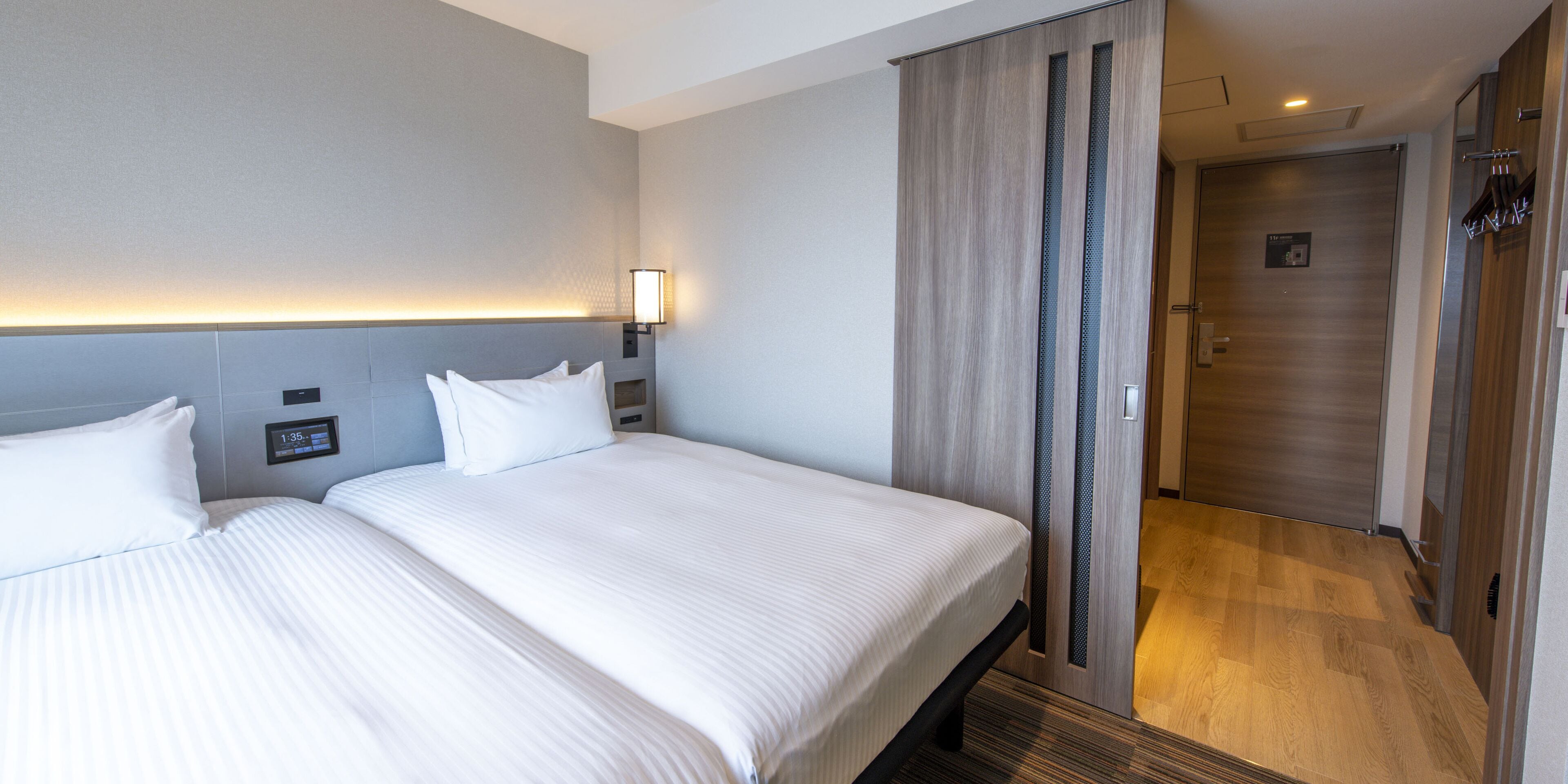 Una habitación de hotel con dos camas, una mesita de noche con lámpara y suelo de madera.