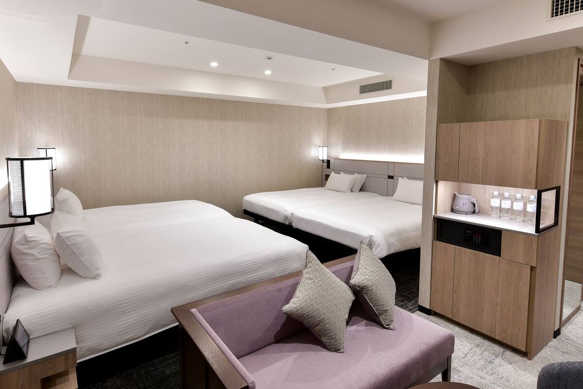 A hotel room with two beds, a sofa, a desk with a computer, and a minibar.