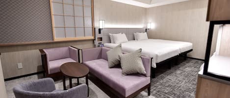 A hotel room with a bed, a sofa, a chair, a small table, and a wall-mounted TV.