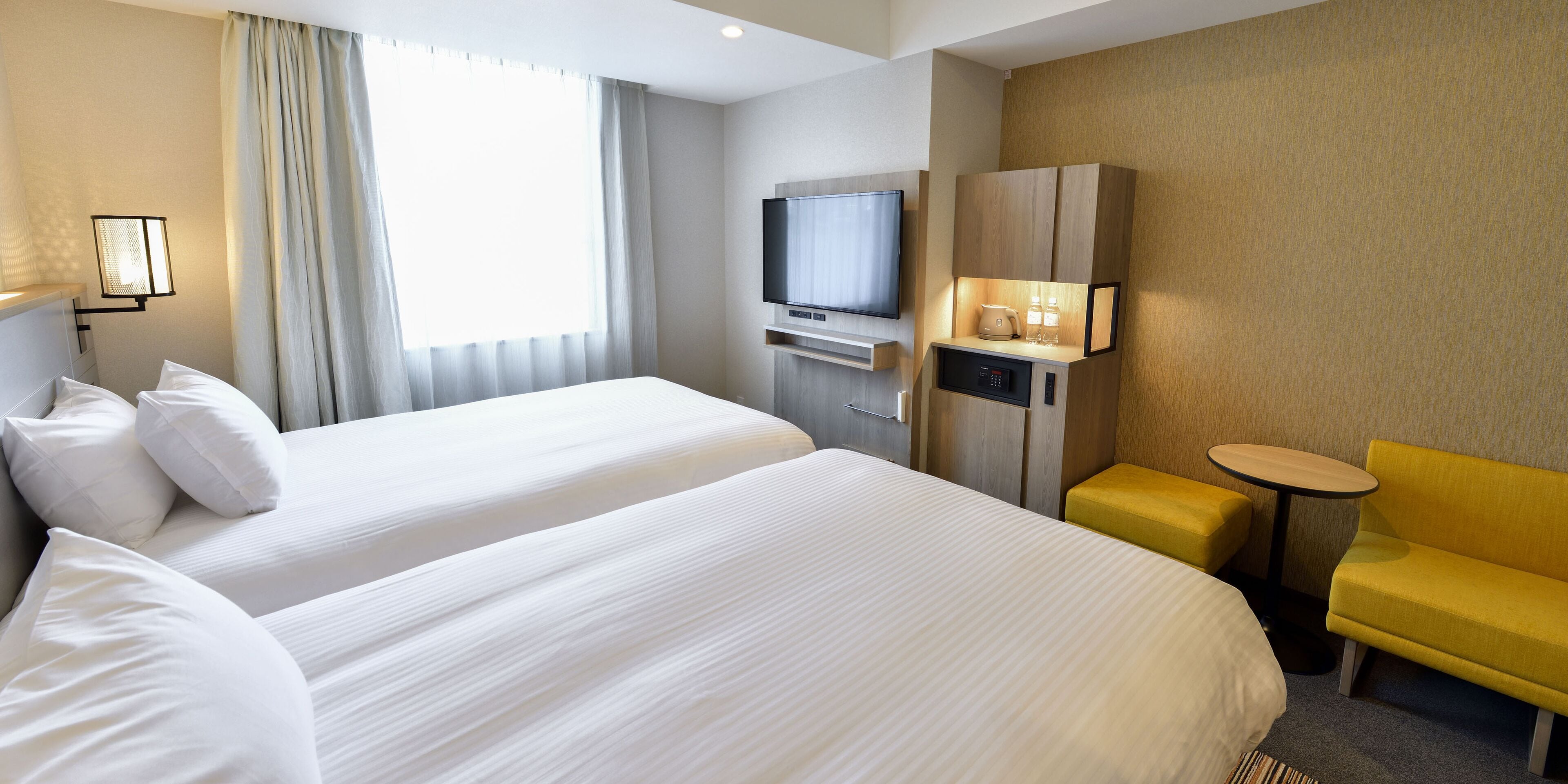 Quarto de hotel com duas camas, televisão, minibar e um pequeno espaço de estar.