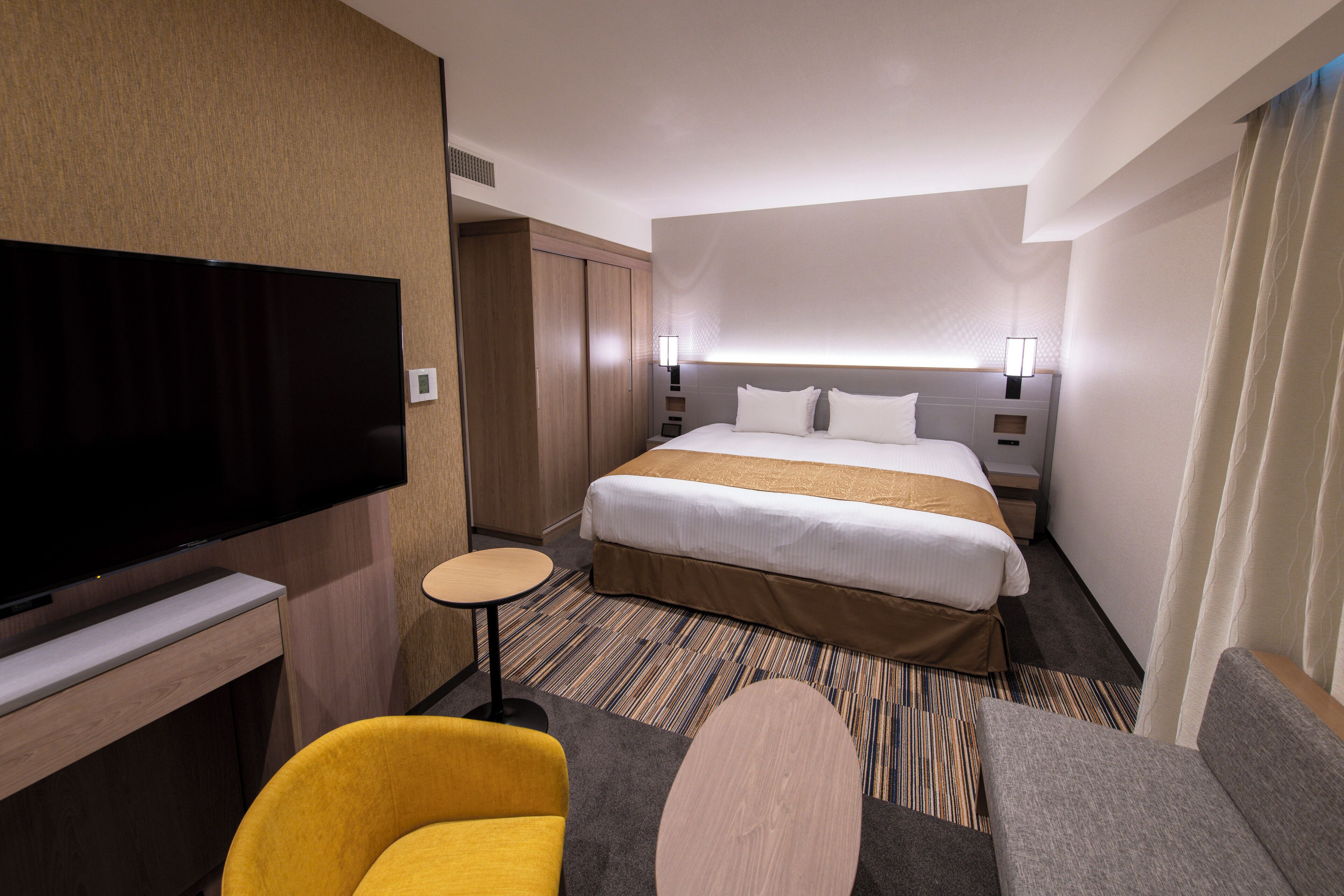 A hotel room with a large bed, a flat-screen TV, a small round table, and a sofa.