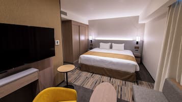 A hotel room with a large bed, a flat-screen TV, a small round table, and a sofa.