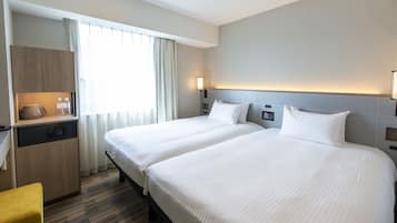 A hotel room with two beds, a desk, a coffee maker, and a window with curtains.