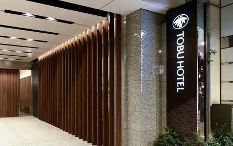 A modern hotel entrance with a wooden panel design, a sign for the Tobu Hotel, and a glass door leading inside.