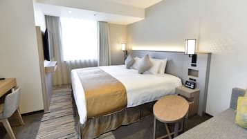 A hotel room with a bed, bedside tables, a desk, a chair, and a small stool.