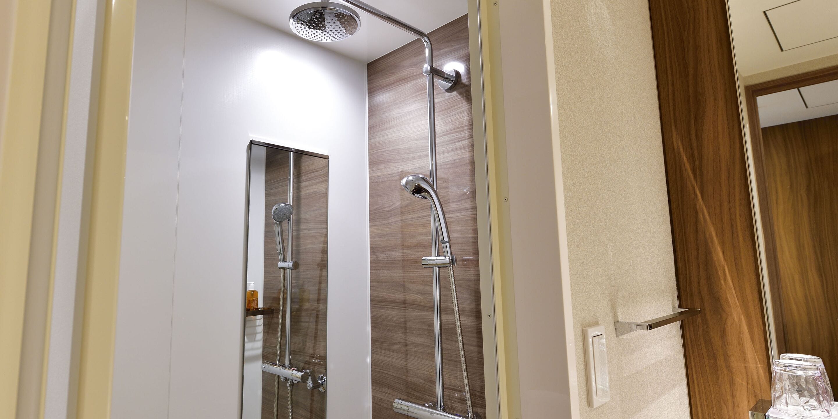 A modern bathroom with a glass shower enclosure, a handheld showerhead, and a wall-mounted faucet.