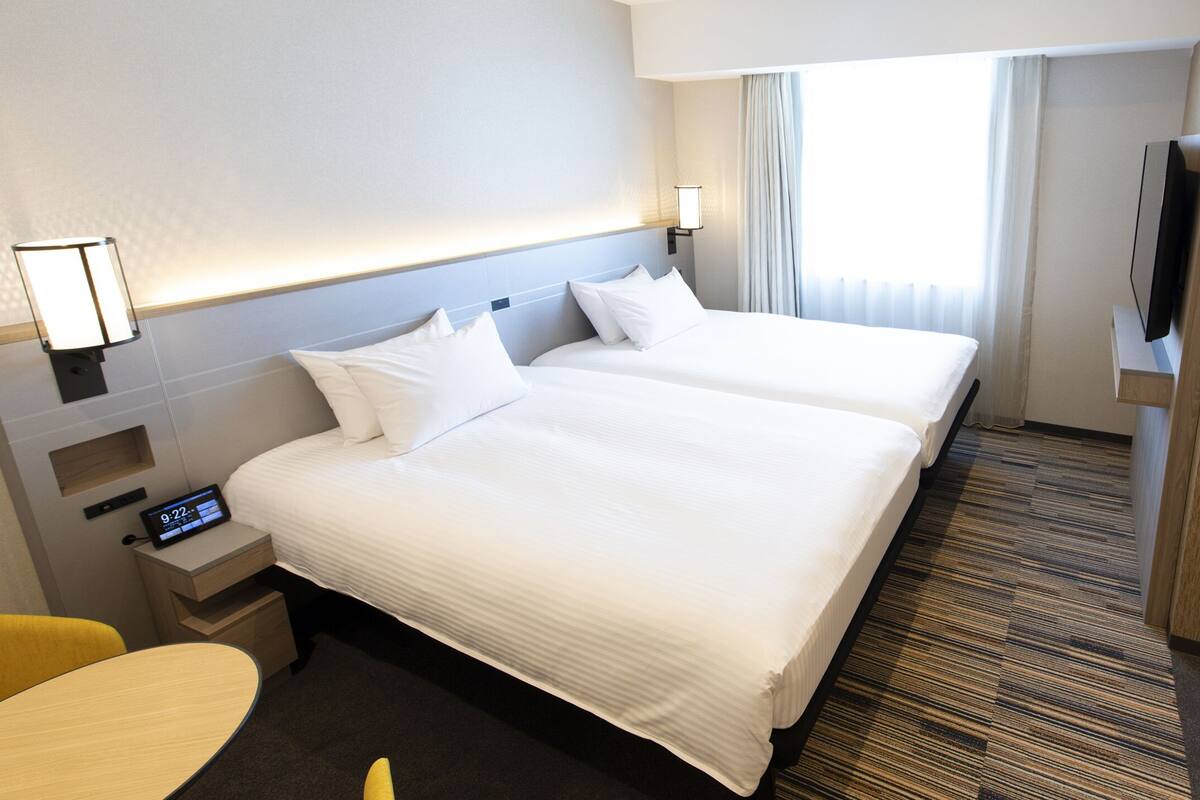 A hotel room with two beds, a desk, a chair, a TV, and a minibar.