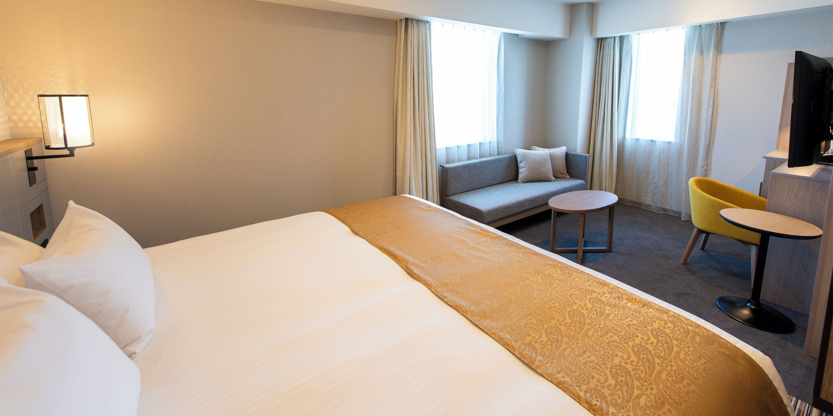 Une chambre d’hôtel avec un grand lit, un canapé, une petite table ronde, une chaise jaune et un téléviseur.