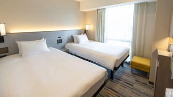 Habitación de hotel con dos camas, un escritorio, una silla y una ventana con cortinas.